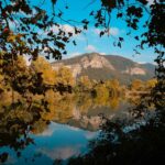 Picturesque scenery of calm lake reflecting mountains and trees with autumnal foliage in sunny day with blue cloudy sky