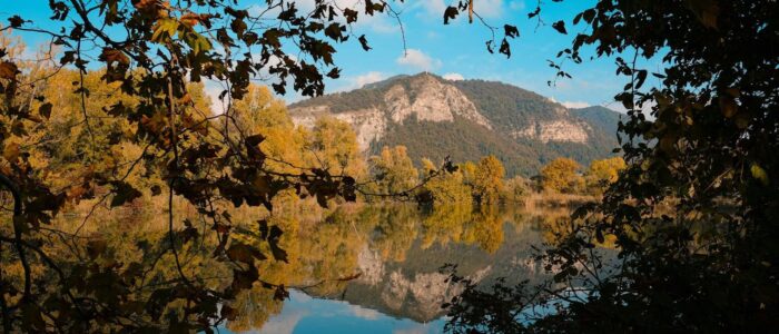 Picturesque scenery of calm lake reflecting mountains and trees with autumnal foliage in sunny day with blue cloudy sky