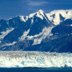 Snow-capped mountains and glacier under blue sky.